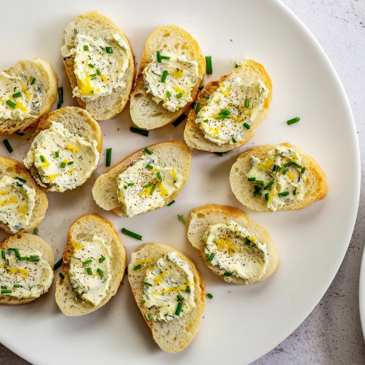 Golden-brown vodka butter crostini spread on a baking sheet, with lemon zest and chives garnish.