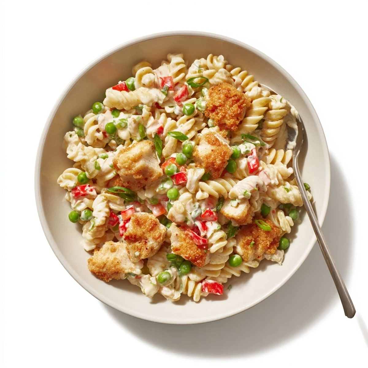 A close-up of Crispy Chicken Ranch Pasta Salad showing golden panko-crusted chicken pieces tossed with rotini pasta, green peas, and diced red bell pepper in a creamy ranch dressing.