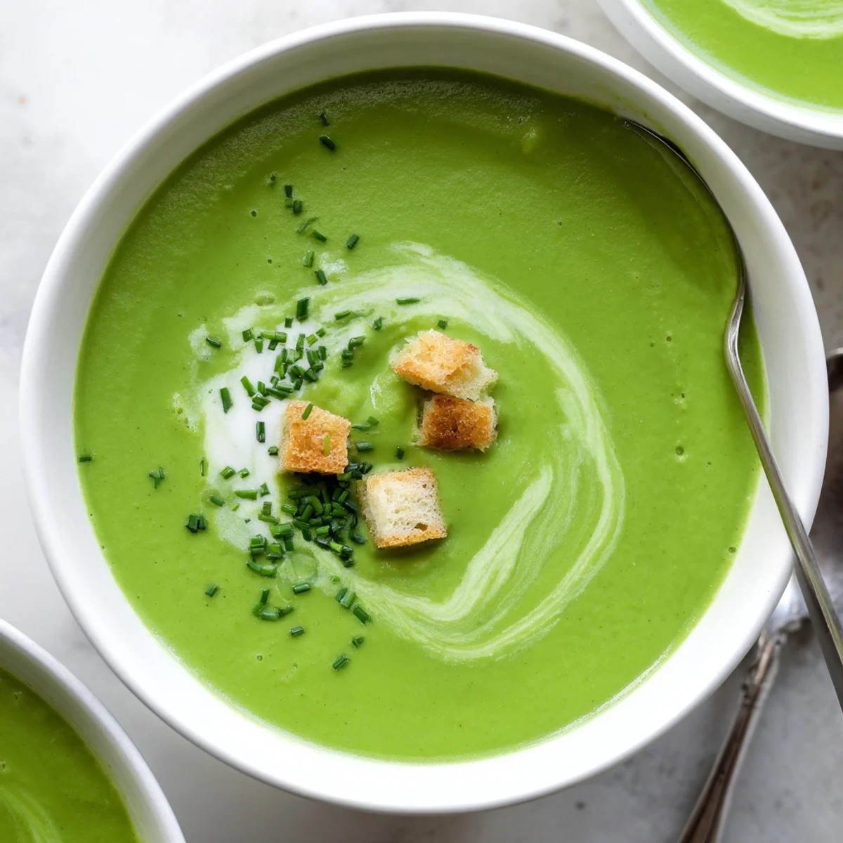 A ladle of hot creamy broccoli soup pours into a bowl, steam rising beside a slice of bread.