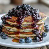 Stack of fluffy High-Protein Greek Yogurt Pancakes drizzled with blueberry compote and a dollop of Greek yogurt.