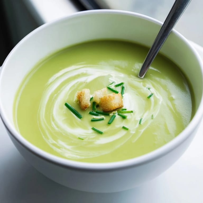 This vibrant bowl of creamy broccoli soup features a velvety green texture and a rustic crouton garnish.